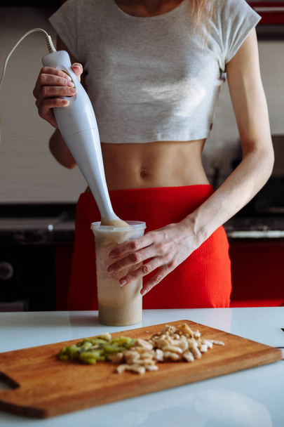 Woman with hand blender making sweet banana protein shake - Foto, afbeelding