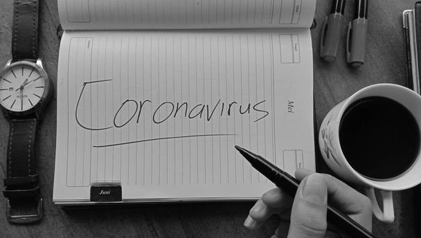WONOSOBO, INDONESIA - Apr 06, 2021: A hand holding a marker and a copybook with the word "Coronavirus" on it in grayscales - Foto, afbeelding