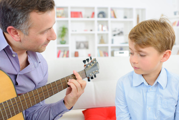 a man is teaching guitar playing to his son - Foto, afbeelding