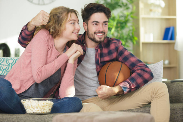 young couple watching the basketball game on tv - Фото, изображение