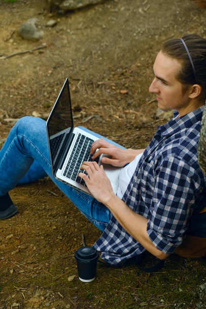 Человек сидит на земле в лесу и работает на ноутбуке - Фото, изображение