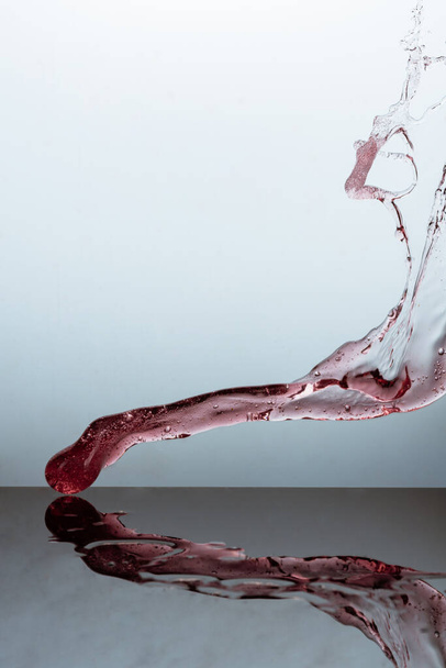 A vertical shot of wine splashing on a reflective glass surface against a gray background - Foto, Bild
