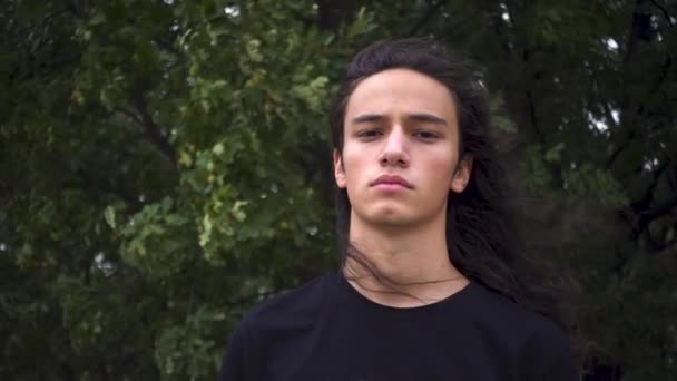 agresszív kinézetű hosszú fekete hajú fiatal tiltakozó férfi áll mogorva előtt drótháló - Felvétel, videó
