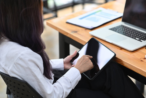 オフィスのデスクに座ってデジタルタブレットを使用している女性オフィスワーカーの背面図. - 写真・画像