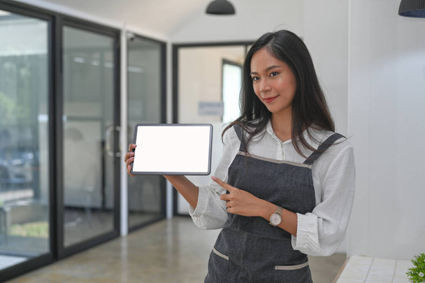 Friendly young woman barista holding and showing digital tablet with empty screen. - Photo, Image
