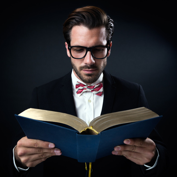 intrigued επιχειρηματίας με γυαλιά, διαβάζοντας ένα βιβλίο. απομονώνονται σε μαύρο. - Φωτογραφία, εικόνα