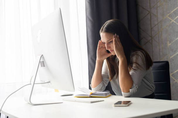 Concentrated upset young woman sitting at the desk in front of PC - Foto, imagen
