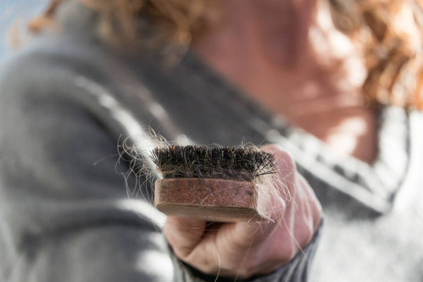 A woman removes hair from a hair brush. - Photo, Image