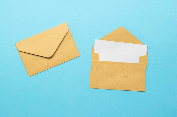 An open postal envelope with a sheet of white paper and a closed envelope on a blue background. The concept of mail correspondence. Flat lay. - Foto, Imagen