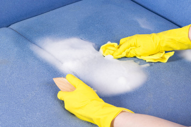 hands in rubber gloves remove the cleaning agent from the upholstered furniture with a rag - Foto, imagen