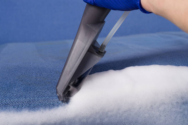 in the hands of an employee of a cleaning company, a vacuum cleaner collects foam for dry cleaning of upholstered furniture, close-up - Foto, Bild