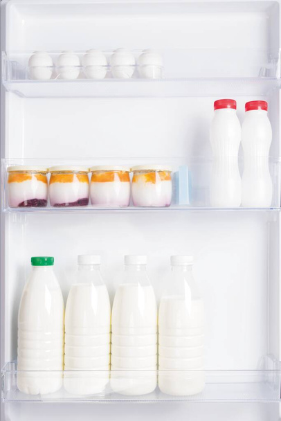 there are dairy products and yoghurts on the shelves in the refrigerator door - Foto, Bild