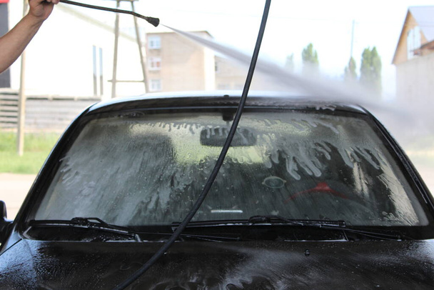 un homme lave indépendamment une voiture kercher / photo un homme lave indépendamment une voiture. Il a un kercher entre les mains. un jet d'eau haute pression. la voiture est noire. - Photo, image