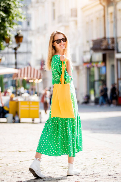 Młoda piękna kobieta z żółtą pościel ekologiczna torba na tle miasta. - Zdjęcie, obraz