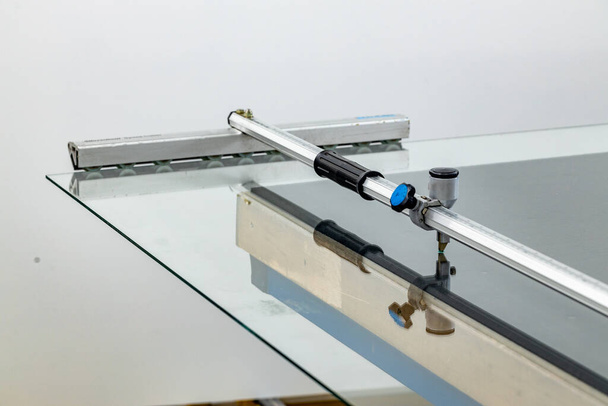 Une grande feuille de verre couchée sur la table dans l'usine de verre et un dispositif spécial pour couper le matériau  - Photo, image