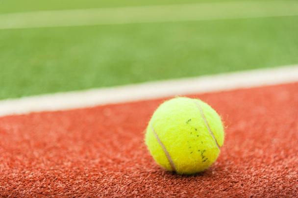 A yellow tennis ball is on the red tennis court. - Photo, Image