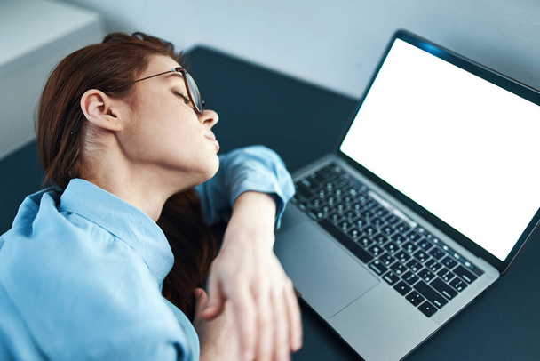 Müde Frau sitzt an einem Tisch vor einem Laptop und arbeitet unzufrieden - Foto, Bild