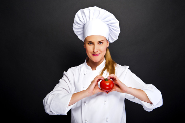 Köchin macht Handherzzeichen mit Tomate vor dunklem Hintergrund - Foto, Bild