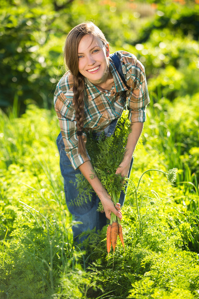 Young woman with a bunch of carrots in the garden - Фото, зображення