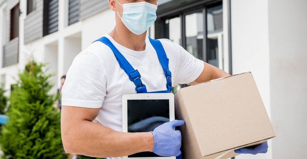 Young courier wearing a protective mask and gloves delivers goods during quarantine - 写真・画像