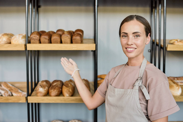 Nuori hymyilevä virkailija osoittaa leipomo valikoima - Valokuva, kuva