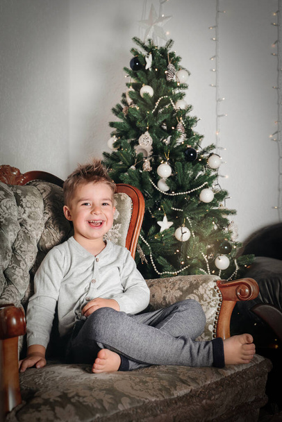 Little boy sitting by Christmas tree. Happy child, Christmas celebration. - Fotó, kép