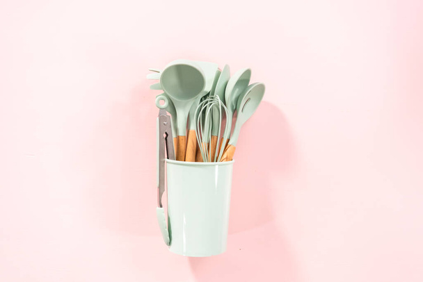 Flat lay. New blue silicone kitchen utensils with wooden handles on a pink background. - Fotó, kép