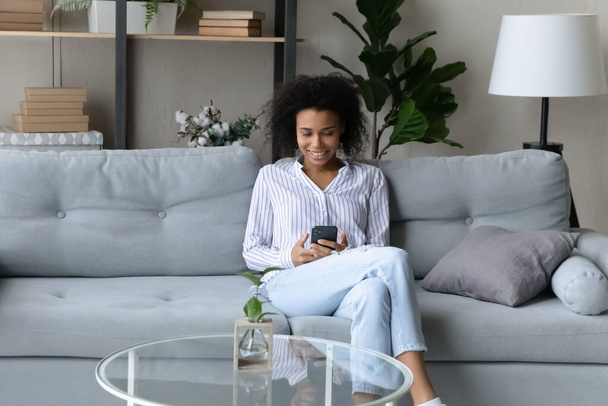 Calm black teen female relax on soft couch using smartphone - Photo, image