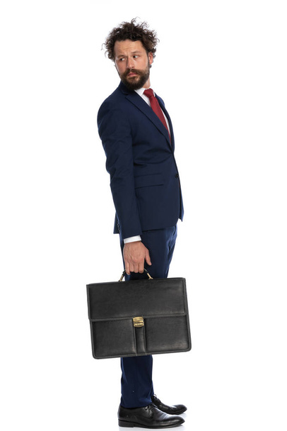 schöner Geschäftsmann blickt über die Schulter und hält eine Aktentasche auf weißem Hintergrund - Foto, Bild