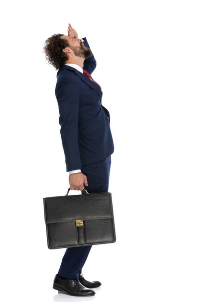 боковой вид красивого бизнесмена, защищающего глаза, чтобы он мог смотреть вверх и держать портфель - Фото, изображение