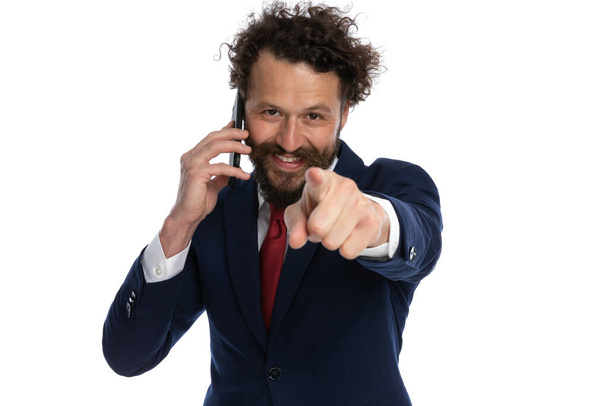 ελκυστικός επιχειρηματίας που δείχνει την κάμερα και μιλάει στο τηλέφωνο σε λευκό φόντο - Φωτογραφία, εικόνα