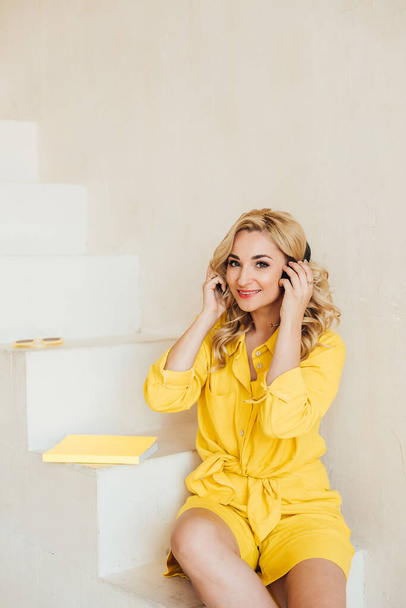 Portrait of a cute, attractive charming woman in a yellow summer suit and headphones listening to music. Soft selective focus. - Foto, afbeelding