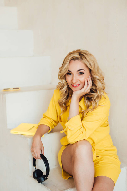 Портрет милой, привлекательной, улыбающейся, очаровательной женщины, смотрящей в камеру в жёлтом летнем костюме с наушниками. Мягкая селективная фокусировка. - Фото, изображение