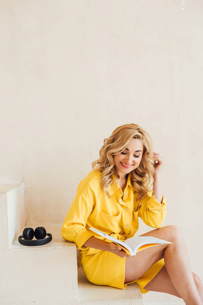 Portret van een leuke, aantrekkelijke, lachende, charmante vrouw in een geel zomerpak met hoofdtelefoon en een geel notitieboekje. Zachte selectieve focus. - Foto, afbeelding