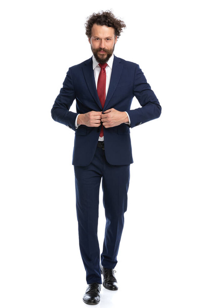 attractive businessman walking towards the camera and fixing his jacket on white background - Foto, Bild
