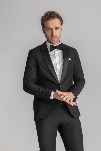 sexy businessman rubbing his palms and wearing a black tuxedo in a fashion pose - Photo, Image