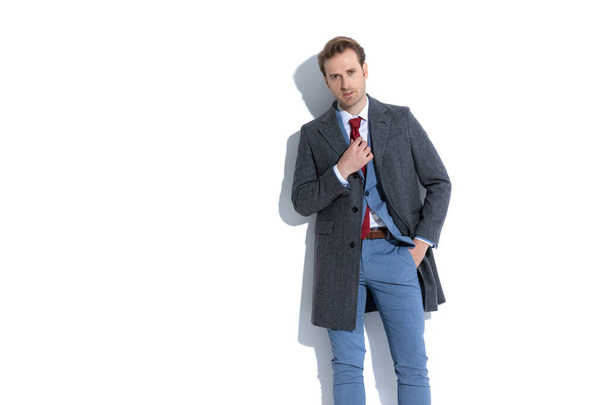 fiatal üzletember rögzíti a nyakkendőjét, és egyik kezét a zsebében fehér háttér - Fotó, kép