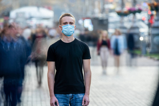 L'homme avec un masque médical sur le visage se tient au milieu du flux humain - Photo, image