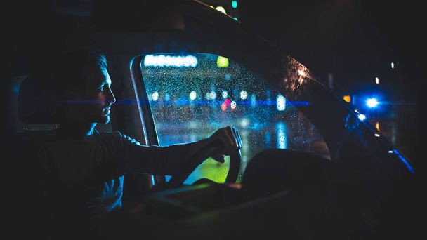 El joven se sienta en el coche en la calle de la noche lluviosa  - Foto, imagen