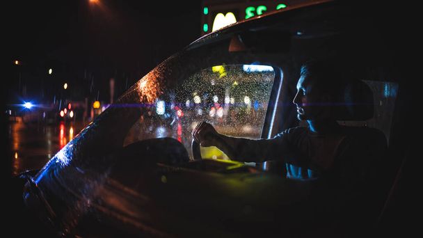 Młody człowiek jeździ samochodem w nocy deszczową drogą. - Zdjęcie, obraz
