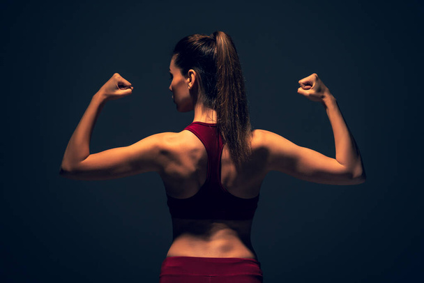 Die schöne Frau in Sportbekleidung demonstriert ihren starken Rücken und Bizeps - Foto, Bild