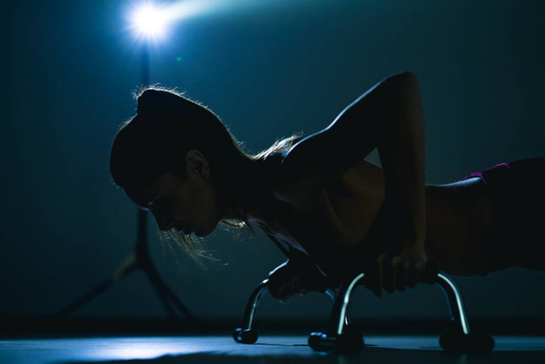 Молодая фитнес-женщина стоит на горизонтальной доске в темной комнате - Фото, изображение