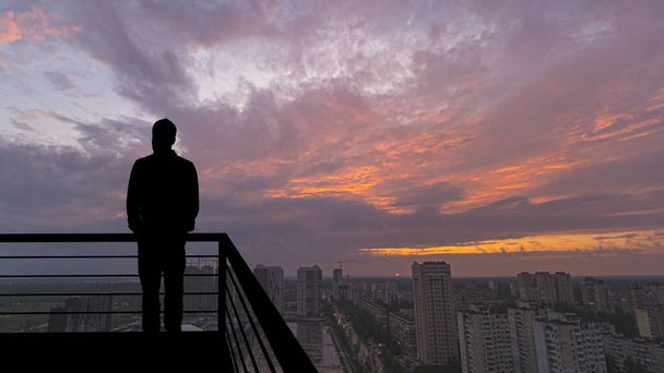 Чоловік стоїть на балконі на великому міському тлі
 - Фото, зображення