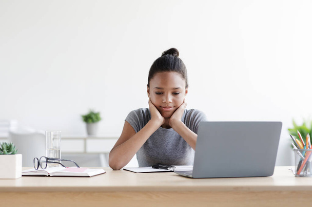 Усталая задумчивая молодая черная девушка отдыхает, обдумывает задание за ноутбуком, учится дома - Фото, изображение