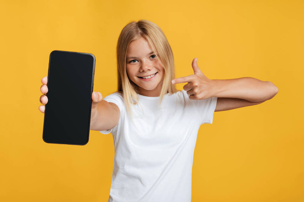 Feliz linda chica rubia adolescente europea muestra el dedo en el teléfono inteligente con pantalla en blanco - Foto, Imagen