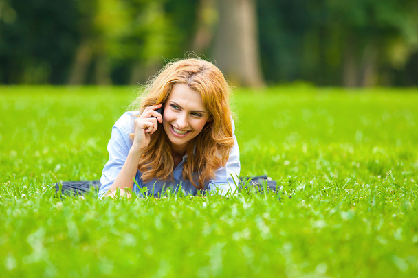 Blonde woman speaking at cellphone in green grass - Fotó, kép