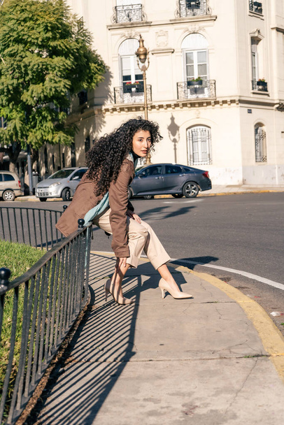 Beautiful Latin woman sitting on a railing in the street. Copy space. - 写真・画像