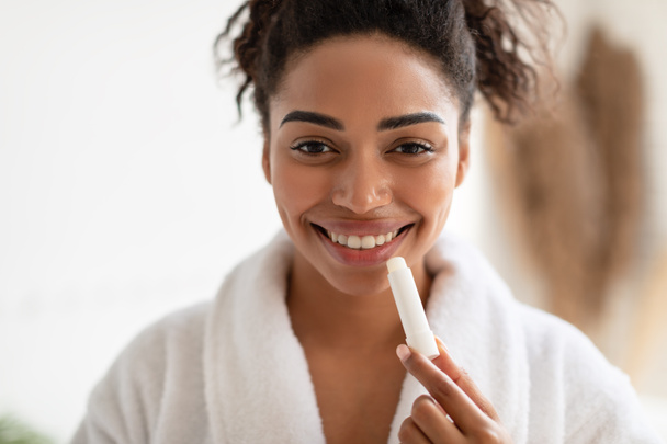 Ritratto di donna nera che applica balsamo labbra in bagno - Foto, immagini