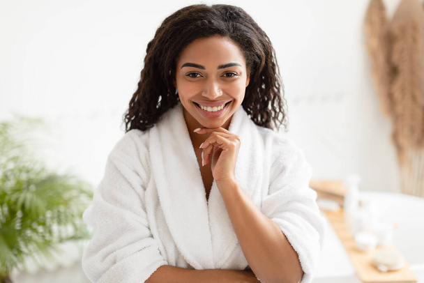 Señora negra posando usando albornoz blanco tocando la barbilla en el baño - Foto, imagen