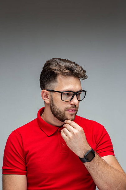 Handsome pensive young male businessman in glasses touching chin thinking, studio portrait on gray with copy space - Fotografie, Obrázek
